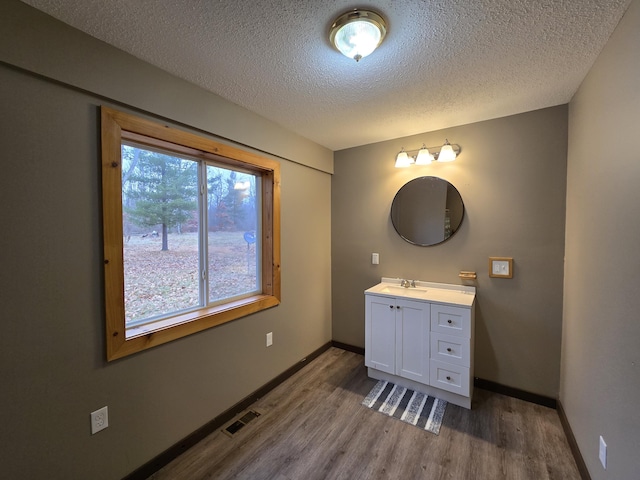 bathroom with a textured ceiling, wood finished floors, visible vents, and baseboards