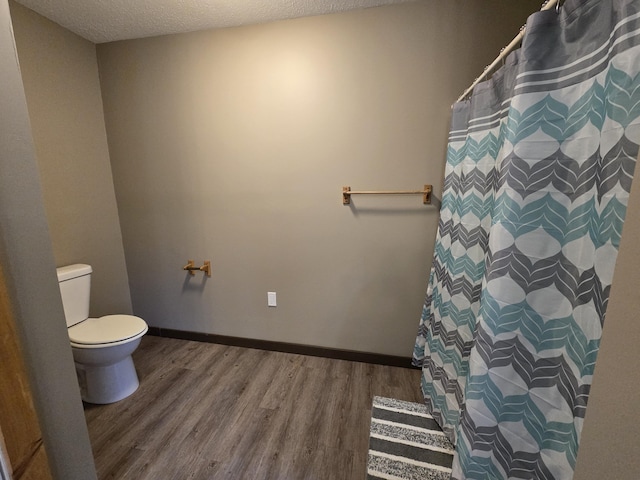 full bathroom featuring toilet, wood finished floors, baseboards, and a textured ceiling