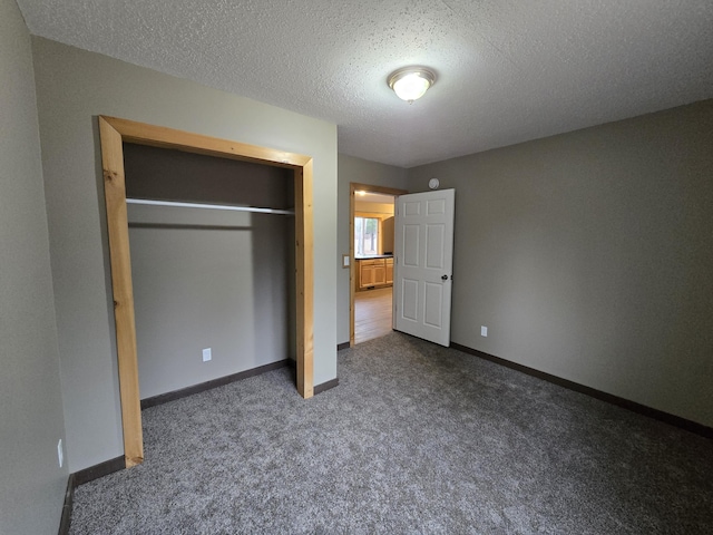 unfurnished bedroom with dark colored carpet, a closet, baseboards, and a textured ceiling