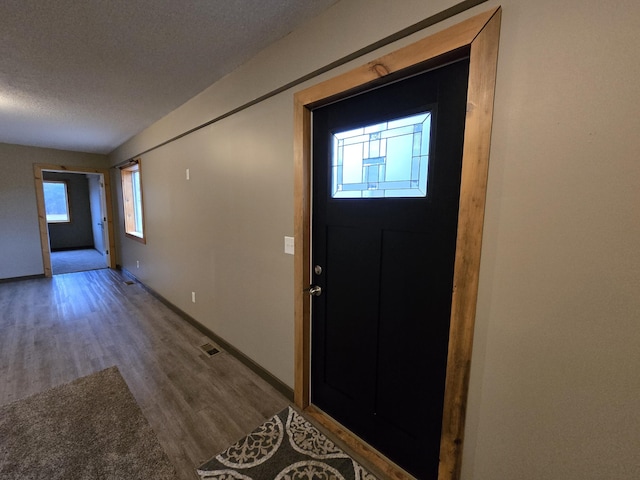 entryway with visible vents, a textured ceiling, baseboards, and wood finished floors