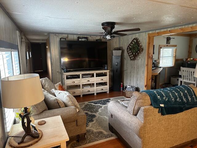 living area featuring wooden walls, a textured ceiling, ceiling fan, and wood finished floors