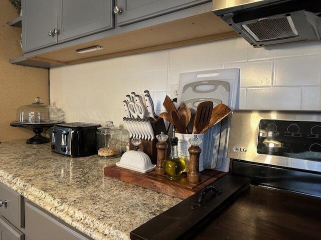 interior details with tasteful backsplash, gray cabinets, light stone countertops, and exhaust hood