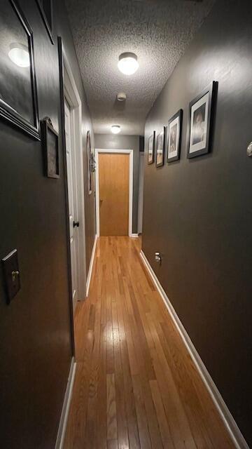 corridor with light wood-style floors, baseboards, and a textured ceiling