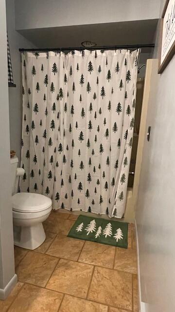 full bathroom featuring a shower with curtain, toilet, and stone finish flooring