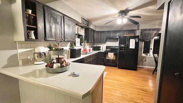 kitchen with light wood finished floors, ventilation hood, light countertops, a textured ceiling, and black appliances