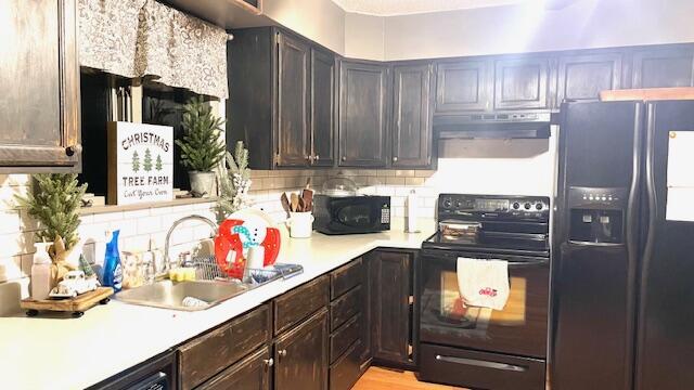 kitchen featuring black appliances, a sink, under cabinet range hood, tasteful backsplash, and light countertops