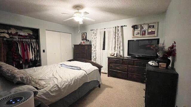 bedroom featuring a textured ceiling, a ceiling fan, multiple closets, and light carpet