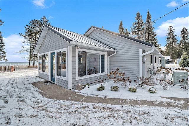 view of snow covered exterior with a standing seam roof, fence, a sunroom, and metal roof