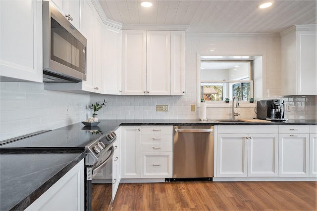 kitchen with dark countertops, backsplash, light wood-type flooring, stainless steel appliances, and white cabinetry