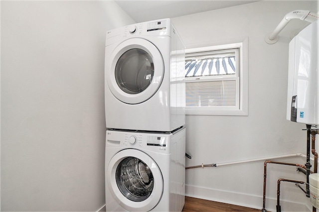 laundry room featuring laundry area, wood finished floors, stacked washer / drying machine, and baseboards