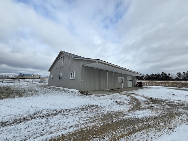 snow covered property featuring an outbuilding, fence, and a garage