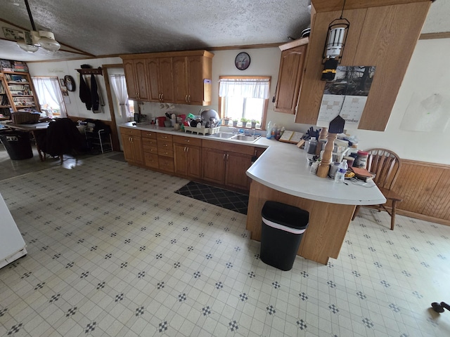 kitchen with a wainscoted wall, ornamental molding, a textured ceiling, light countertops, and light floors