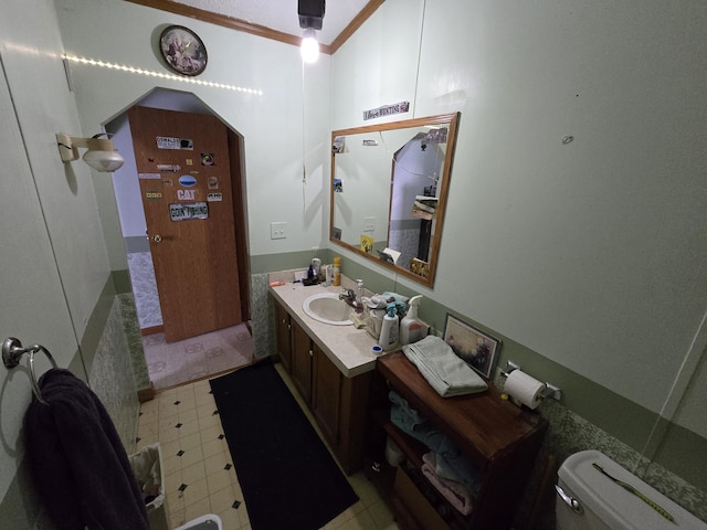 half bath with vanity, crown molding, toilet, and tile patterned floors