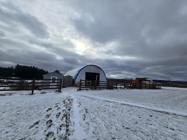 snow covered structure with an outbuilding, fence, and a pole building