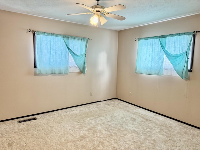 carpeted empty room featuring a textured ceiling, a ceiling fan, visible vents, and baseboards