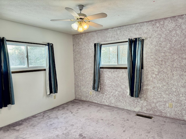 unfurnished room with carpet flooring, a ceiling fan, visible vents, and a textured ceiling