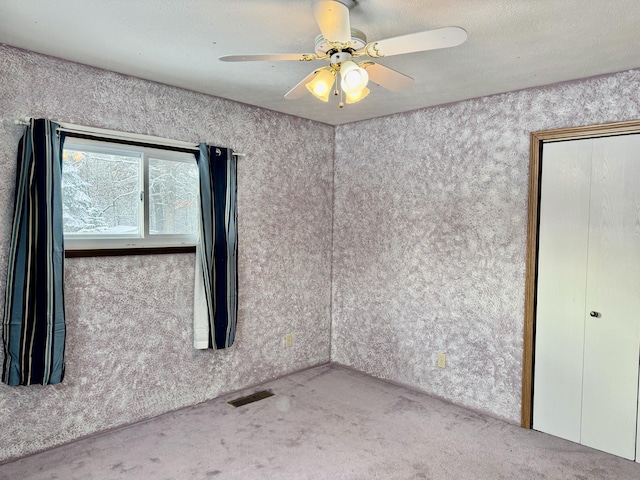 carpeted spare room featuring visible vents and ceiling fan