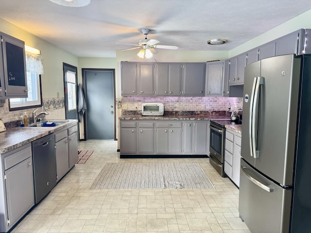 kitchen featuring a sink, stainless steel appliances, dark countertops, and gray cabinetry