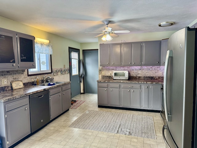 kitchen with gray cabinets, a sink, black dishwasher, dark countertops, and freestanding refrigerator