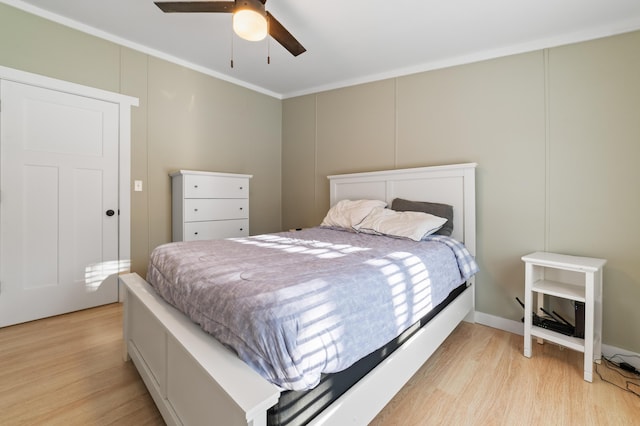 bedroom with light wood finished floors, a decorative wall, a ceiling fan, and ornamental molding