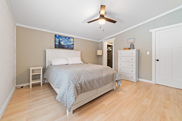 bedroom with a walk in closet, ornamental molding, a ceiling fan, wood finished floors, and vaulted ceiling