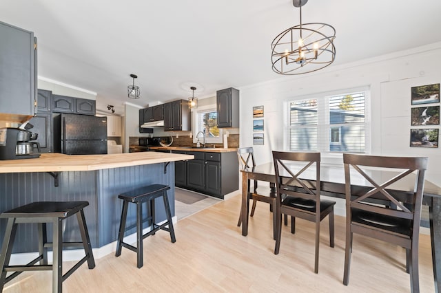 kitchen featuring light wood finished floors, a peninsula, a kitchen breakfast bar, freestanding refrigerator, and hanging light fixtures