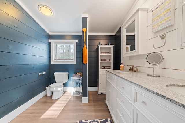 bathroom featuring wood finished floors, baseboards, double vanity, a sink, and toilet