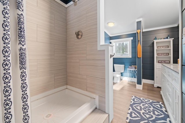 bathroom featuring toilet, wood finished floors, vanity, and a tile shower