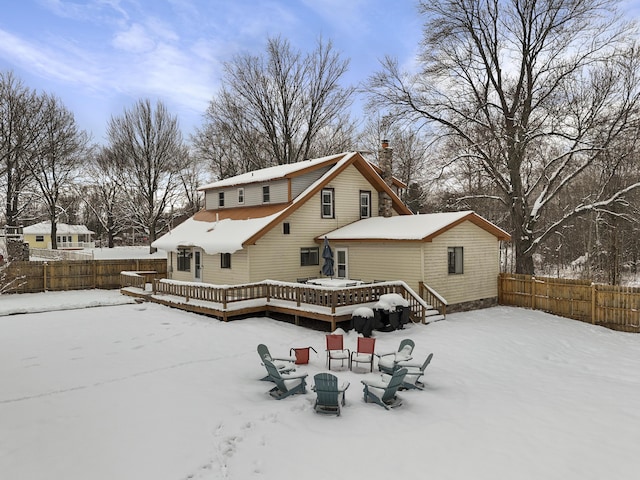 snow covered back of property with a fire pit, a deck, and fence