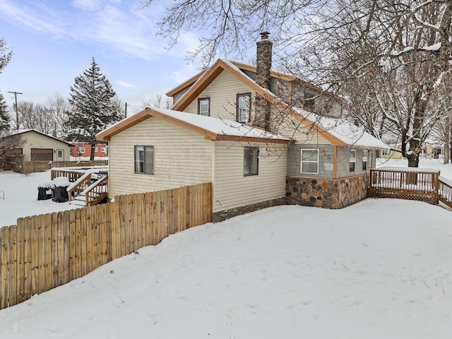 snow covered rear of property with a garage, a chimney, a deck, and fence