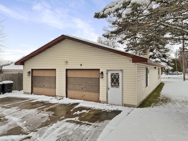 snow covered garage featuring a garage and fence