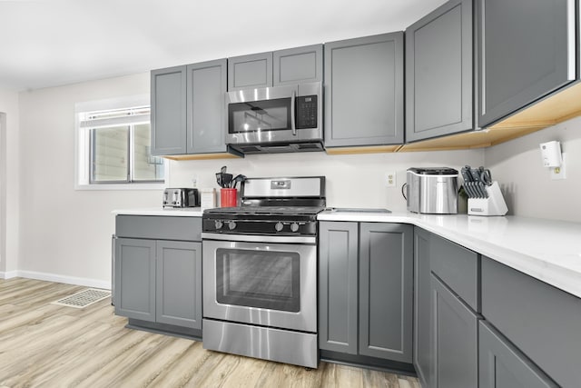 kitchen featuring light countertops, light wood-style floors, appliances with stainless steel finishes, and gray cabinetry