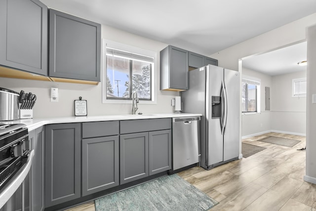 kitchen with light wood-style flooring, appliances with stainless steel finishes, gray cabinetry, and a sink