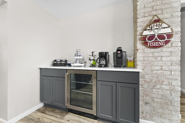 bar with wine cooler, light wood finished floors, a bar, and baseboards