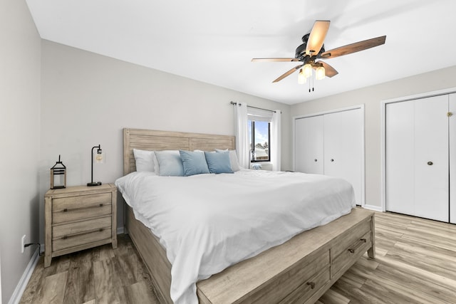 bedroom with a ceiling fan, wood finished floors, multiple closets, and baseboards