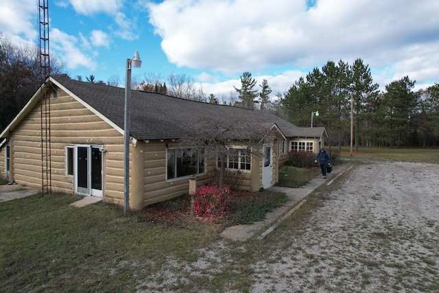 rear view of property with log veneer siding, a lawn, and a shingled roof