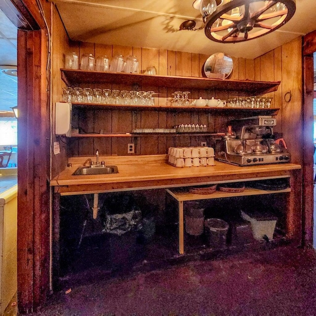 bar featuring a sink, an inviting chandelier, wood walls, carpet flooring, and indoor wet bar