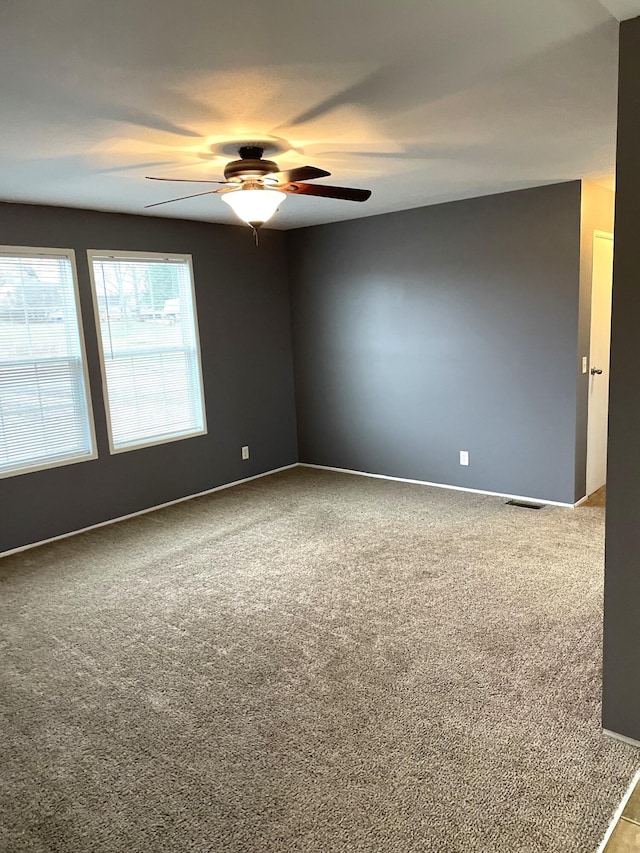 carpeted spare room featuring visible vents, baseboards, and ceiling fan