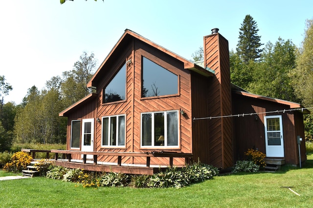 rear view of property with a deck, entry steps, a chimney, and a yard