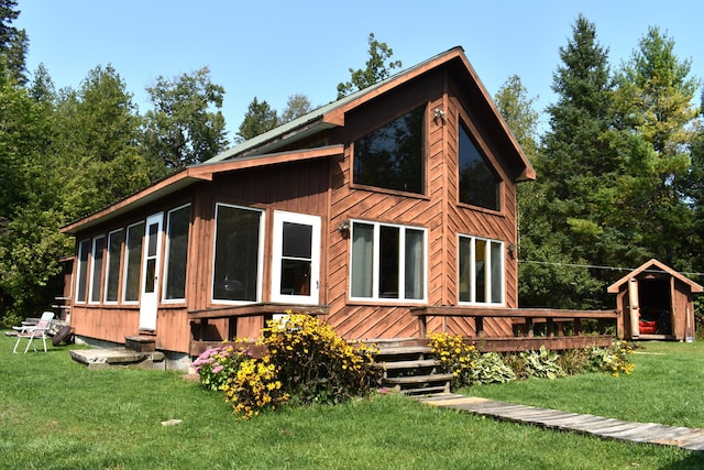 rear view of property with a deck, a lawn, and a sunroom