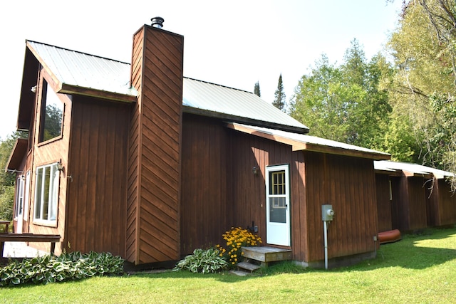 view of property exterior featuring a lawn, a chimney, and metal roof