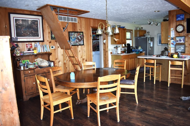 dining space with visible vents, a chandelier, wood walls, dark wood-style floors, and a textured ceiling