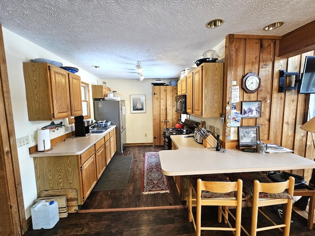 kitchen featuring a kitchen breakfast bar, dark wood finished floors, a peninsula, appliances with stainless steel finishes, and light countertops