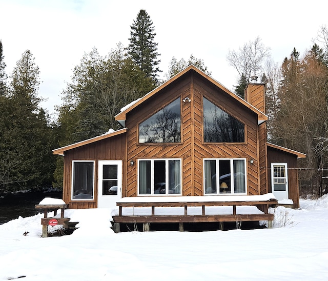 snow covered back of property featuring a wooden deck, board and batten siding, and a chimney