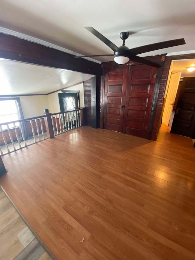 empty room with plenty of natural light, beam ceiling, wood finished floors, and a ceiling fan