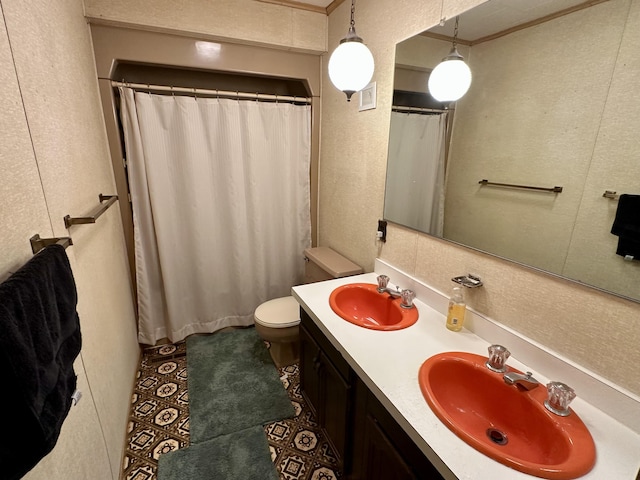 bathroom with double vanity, toilet, a textured wall, and a sink