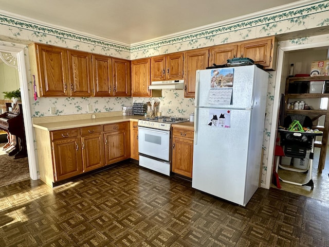 kitchen with gas stove, wallpapered walls, freestanding refrigerator, light countertops, and under cabinet range hood