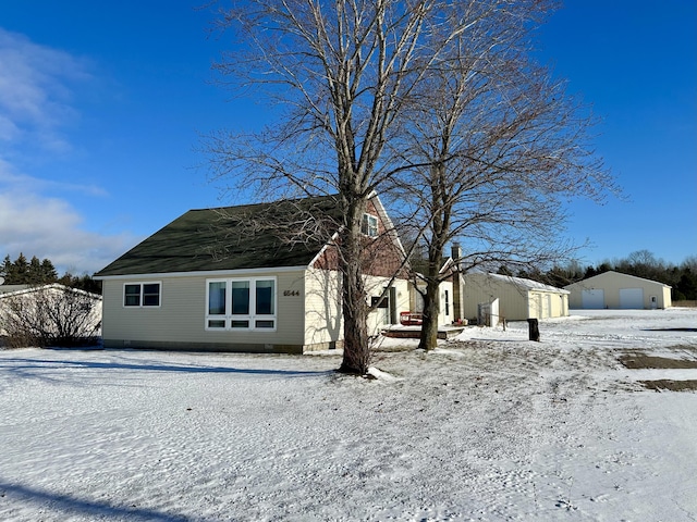 snow covered rear of property featuring a detached garage and an outdoor structure