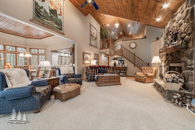 carpeted living room with a stone fireplace, stairs, wood ceiling, and a towering ceiling