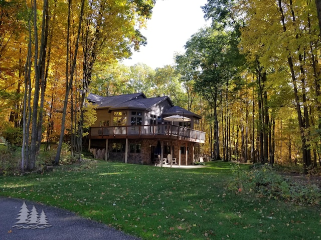 back of house with a deck, a yard, a view of trees, and stone siding